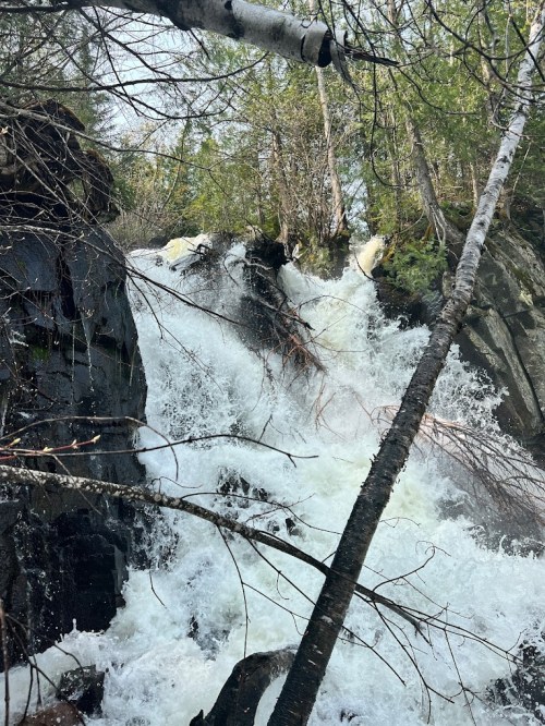 A cascading waterfall surrounded by rocky terrain and trees, with rushing water and splashes visible.