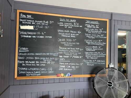 Chalkboard menu featuring raw bar items, soups, salads, and sandwiches with prices listed.