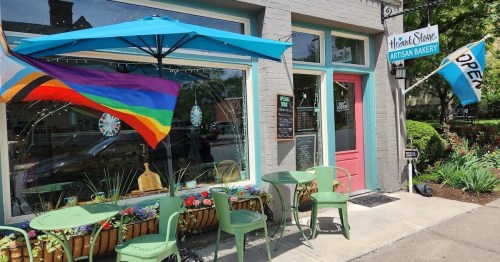 A colorful bakery exterior with outdoor seating, featuring a rainbow flag and an "Open" sign.