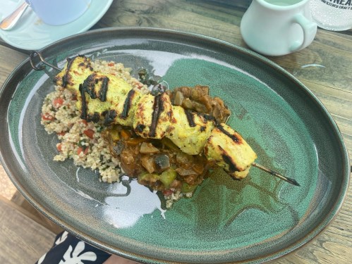 Grilled chicken skewer on a bed of couscous with mixed vegetables, served on a green plate.