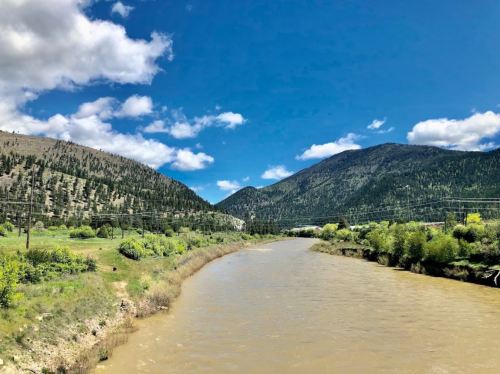 A winding river flows through a lush green valley, surrounded by mountains under a bright blue sky with fluffy clouds.