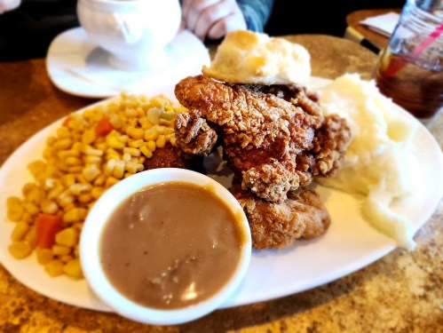 A plate of fried chicken with a biscuit, corn, mashed potatoes, and gravy on a table.