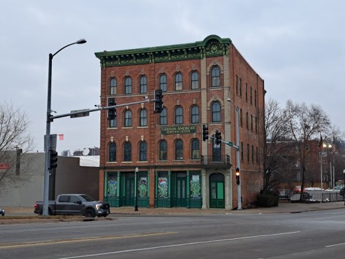 Historic brick building with green accents, featuring decorative windows and signage, located at a street intersection.