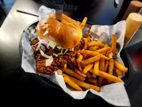 A crispy chicken sandwich with lettuce and onions, served with a side of golden French fries in a black basket.