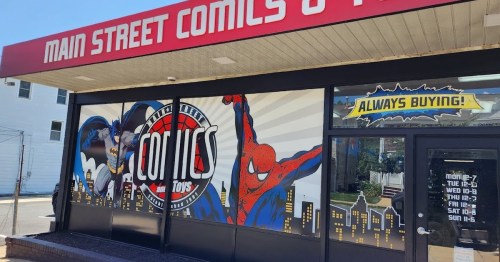 Storefront of Main Street Comics featuring superhero murals of Batman and Spider-Man, with a sign saying "Always Buying!"