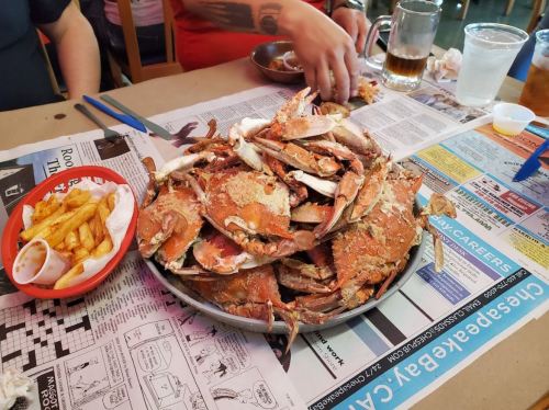 A large platter of crabs sits on a table covered with newspapers, alongside fries and drinks.