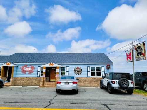 A blue building with a sign reading "Rambo's" and a diving flag, featuring parked cars in front under a cloudy sky.