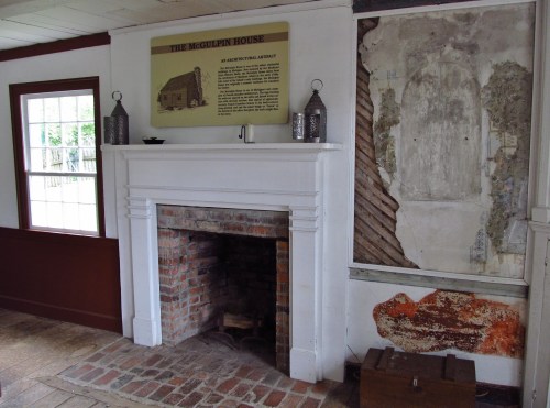 Interior of the McGulpin House featuring a brick fireplace, historical sign, and exposed wall with peeling paint.