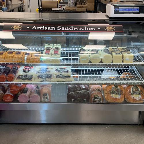 Display case filled with various artisan sandwiches and cheeses, labeled "Artisan Sandwiches" at the top.