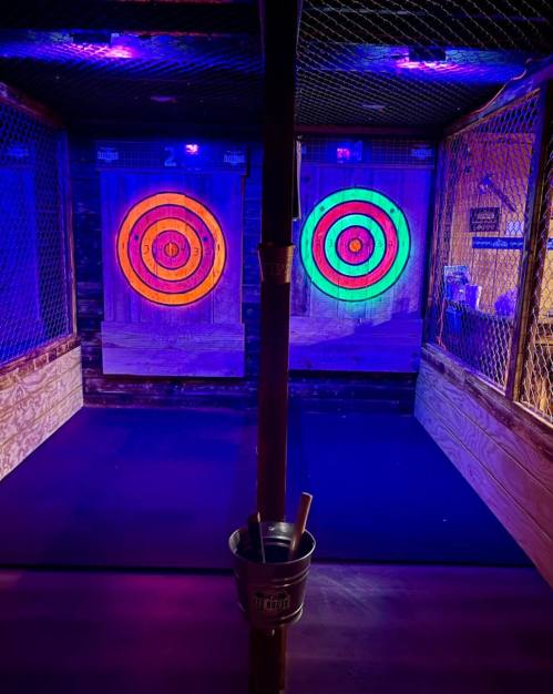 Two illuminated dartboards in a dimly lit space, with vibrant colors and a wooden floor. A bucket is in the foreground.