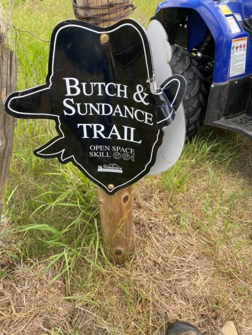 Sign for "Butch & Sundance Trail" with a cowboy hat design, located near an ATV in a grassy area.