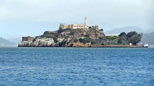 A distant view of Alcatraz Island with its historic buildings surrounded by water under a cloudy sky.