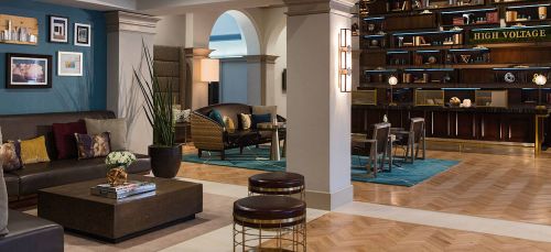 Modern hotel lobby featuring stylish seating, decorative plants, and a well-lit reception area with a "High Voltage" sign.