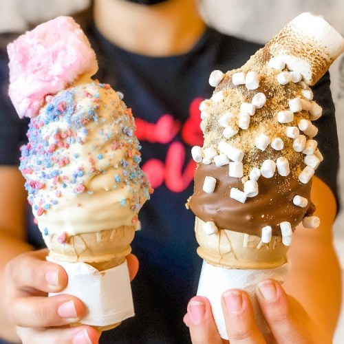 Two ice cream cones with colorful toppings: one with sprinkles and cotton candy, the other with chocolate and marshmallows.