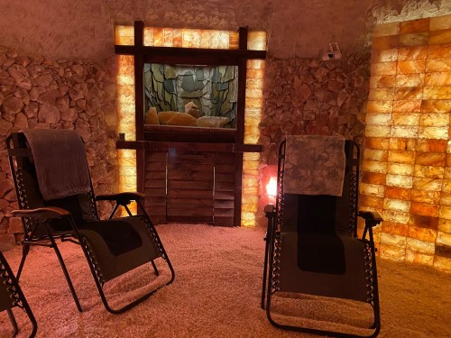 A serene salt room with two reclining chairs, illuminated salt walls, and a calming stone feature in the background.