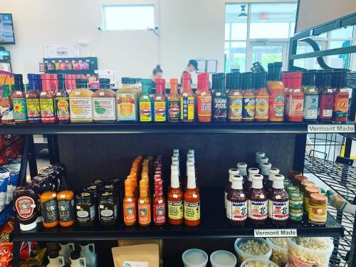 A display of various hot sauces and condiments on shelves in a store, with labels indicating some are Vermont made.