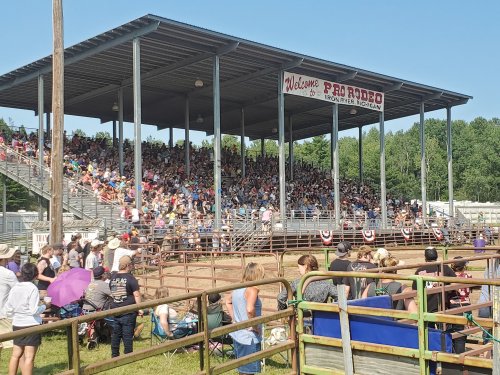 A large crowd gathers under a covered grandstand at a rodeo event, with people seated and enjoying the festivities.