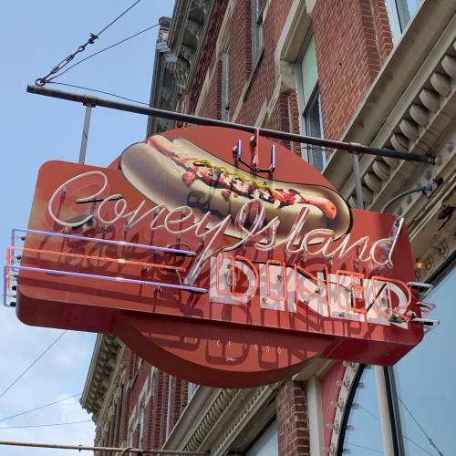 Sign for Coney Island Diner featuring a hot dog graphic, with a bright red background and retro neon lights.