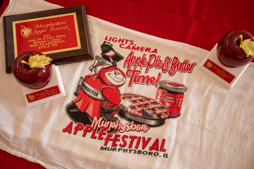 A towel featuring a cartoon chef with apple pie, awards, and a plaque for the Murphysboro Apple Festival.