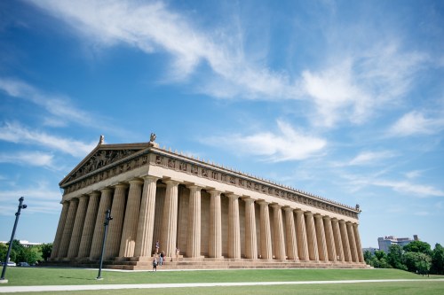 A large classical-style building with tall columns under a blue sky, set in a green landscape.