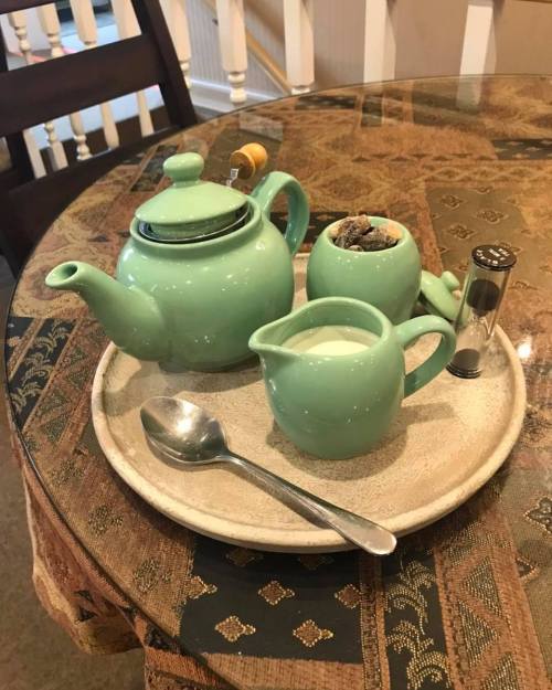 A green teapot, creamer, and sugar bowl on a round tray, placed on a patterned tablecloth.