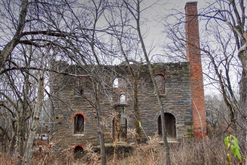 A weathered stone ruin surrounded by bare trees, with a tall brick chimney and broken windows.