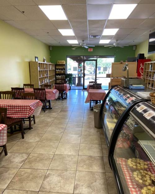 Interior of a cozy café with checkered tablecloths, shelves of goods, and a display case of baked items.