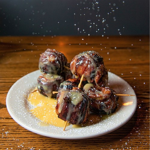 A plate of dessert bites drizzled with glaze and dusted with powdered sugar, set on a wooden table.