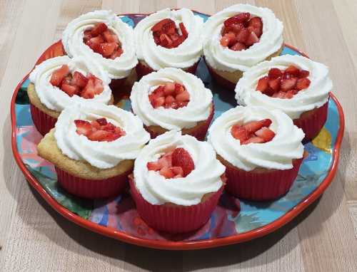 A colorful plate of cupcakes topped with whipped cream and fresh strawberries, arranged in a circular pattern.