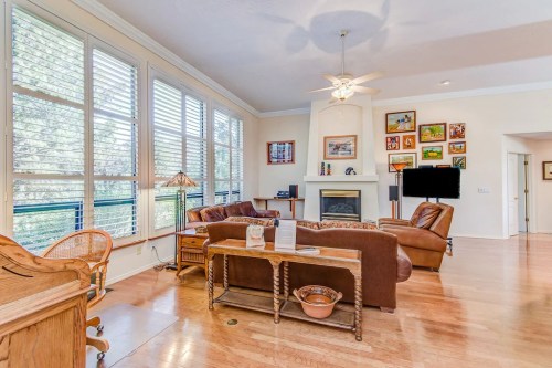 Bright living room with large windows, wooden floors, a fireplace, and cozy furniture. Decorated with framed artwork.