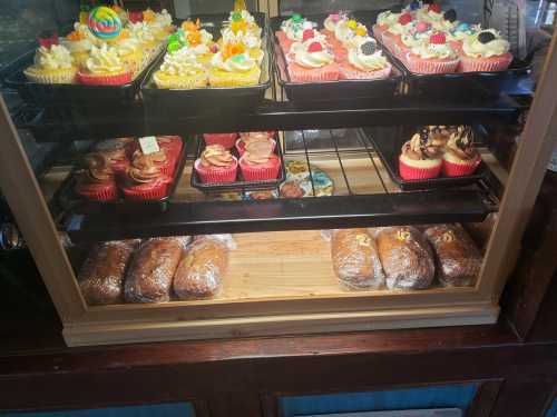 A display case filled with colorful cupcakes and pastries, showcasing various decorated treats and loaves of bread.