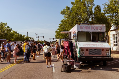 A busy street scene with a food truck named "Bondi Bowls" and a crowd of people enjoying the outdoor event.