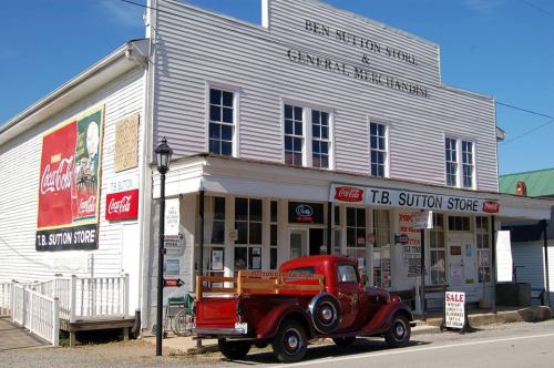 A vintage red truck parked in front of the T.B. Sutton Store, featuring classic Coca-Cola advertisements on the building.