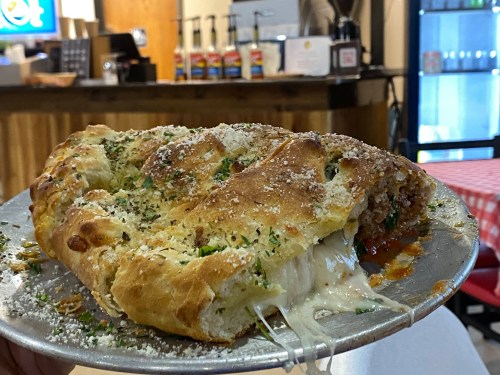 A cheesy calzone on a metal plate, filled with meat and herbs, with a rustic restaurant background.
