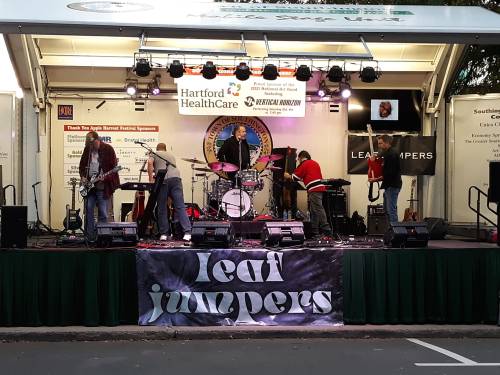 A band setting up on stage with instruments and equipment, featuring a banner that reads "Leaf Jumpers."