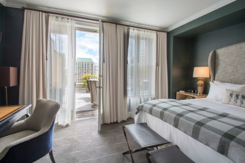 A stylish hotel room with a bed, desk, and balcony doors leading to a view of the outdoors.