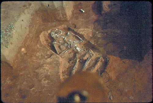 An archaeological excavation showing a partially unearthed ancient burial site with a human figure.