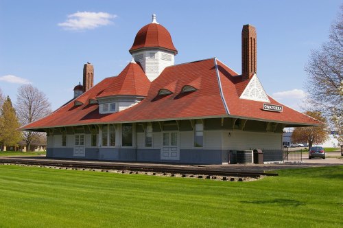 Historic train station with a red roof and unique architectural features, set against a clear blue sky and green grass.