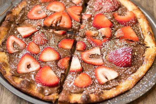A chocolate pizza topped with fresh strawberries and dusted with powdered sugar, sliced into pieces.