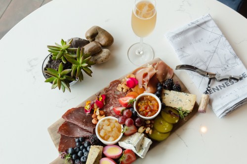 A charcuterie board with meats, cheeses, fruits, and nuts, accompanied by a drink and a small plant on a table.