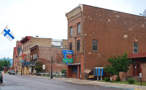 A quiet street scene featuring historic brick buildings, a Finnish flag, and a sign for a local sports bar.