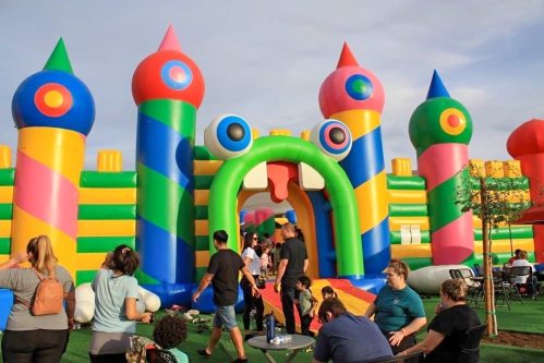 Colorful inflatable bounce house with people playing and enjoying the outdoor space. Brightly decorated with towers.