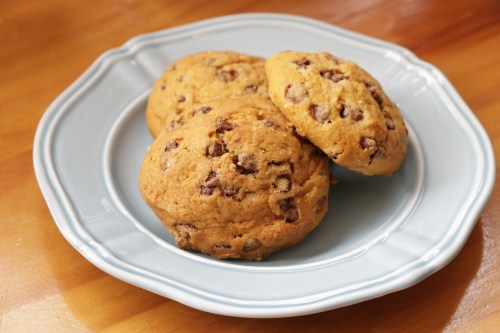 Three chocolate chip cookies on a light blue plate, resting on a wooden surface.