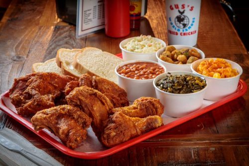 A red tray with fried chicken, two slices of bread, and four sides: coleslaw, baked beans, greens, and macaroni and cheese.