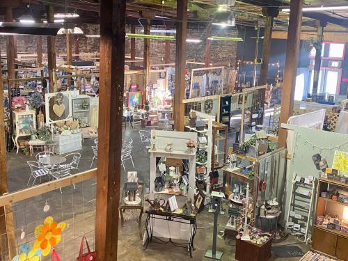 A spacious vintage market filled with various decor items, furniture, and crafts, featuring wooden beams and warm lighting.
