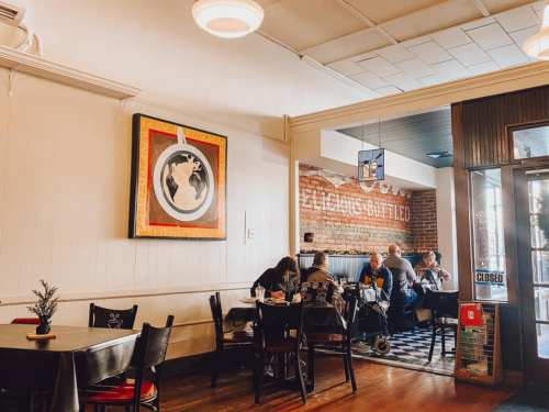 Cozy café interior with patrons at tables, artwork on the wall, and a "CLOSED" sign by the entrance.