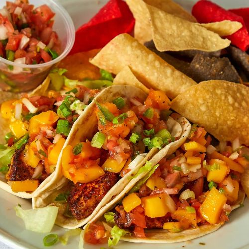 Three tacos topped with fresh salsa and mango, served with tortilla chips and a side of pico de gallo.