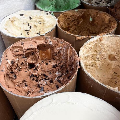 Several ice cream tubs with various flavors, some partially empty, showcasing chocolate, vanilla, and mint green ice cream.