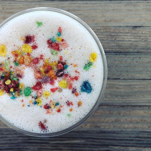 A close-up of a frothy drink topped with colorful candy sprinkles, set against a wooden background.