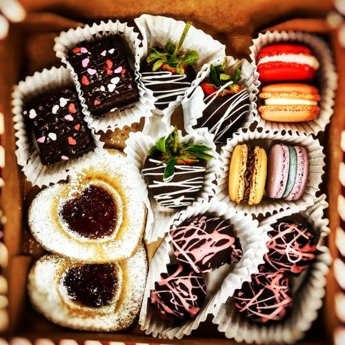 A box of assorted chocolates, including heart-shaped treats, strawberries, macarons, and brownies, beautifully arranged.
